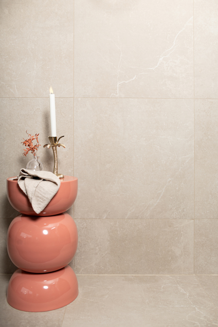 Korallfärgad pall med en ljusstake, torkade växter och duk i beige rum.