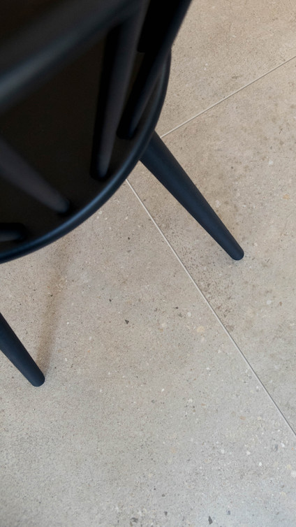 Svart stolsben på beige klinkergolv.