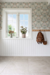 Fönster med krukväxter på fönsterbänk, blommig tapet och väggpanel, ryggsäckar hängande på väggen.