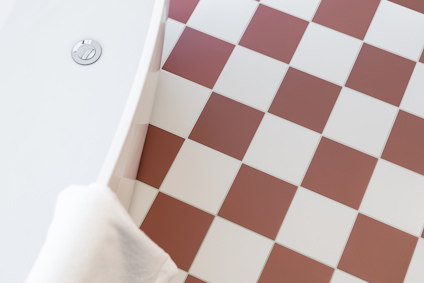Vit och brunvitrutig golvyta bredvid rundad del av ett badkar med en vit handduk.