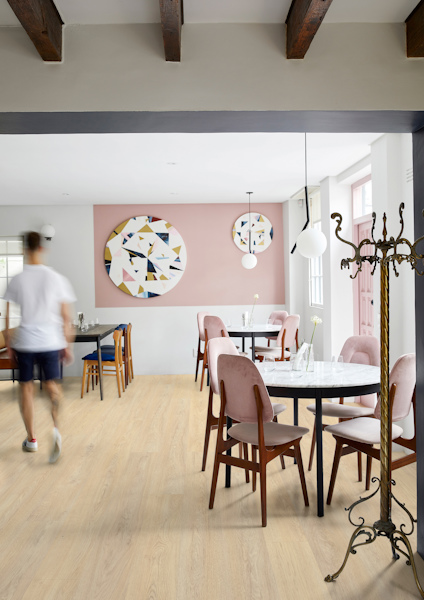En ljus matplats med bord och stolar, väggdekorationer med geometriska mönster och en person som går förbi.