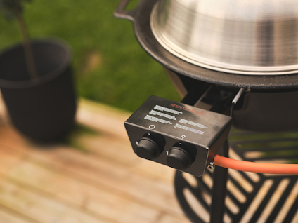 Grill med metallhuv, vred och gasolslang på trätrall. Svart hink i bakgrunden.