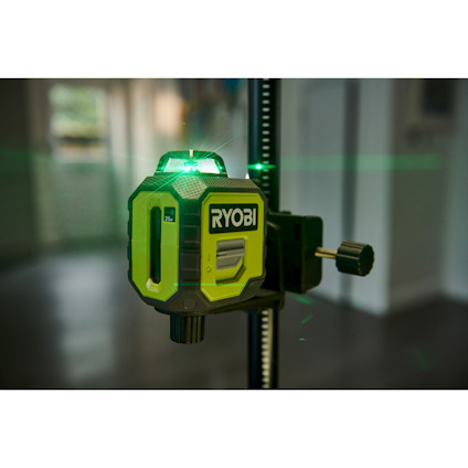 Ryobi grön laserpass med stativinställning inomhus, grön laserlinje synlig mot en oskarp bakgrund av ett rum.