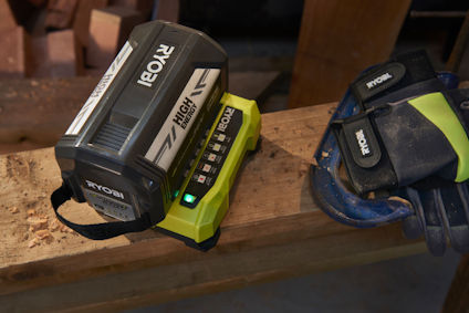 Batteriladdare och batteri från Ryobi placerade på träbänk, med handskar bredvid.