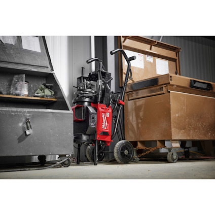 Röd Milwaukee rörpressmaskin på vagn bredvid bruna och grå verktygsskåp i garage eller verkstad.