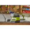 En grön och svart Ryobi batteriladdare med batteri placerad på en arbetsbänk i verkstadsmiljö.
