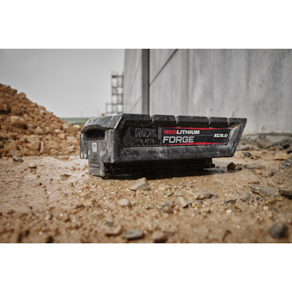 Batteri med texten "Red Lithium Forge XC6.0" på lerig mark vid en betongvägg och jordhög.