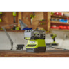 Ryobi batteriladdare och batteri på en arbetsbänk i en verkstad med suddiga verktyg i bakgrunden.