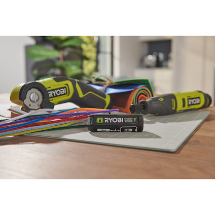 4V USB lithium battteri från Ryobi ligger på ett bord inomhus med en multisax och roterande multiverktyg