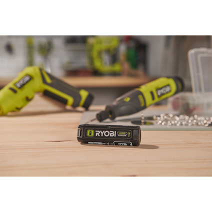 Arbetsbord med verktyg, inklusive en Ryobi-batteriladdare, skruvdragare och spridda skruvar i bakgrunden.