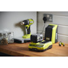 Batteridriven borr, snabbladdare och batteri på träbord med glasburkar och verktyg. Märke: Ryobi