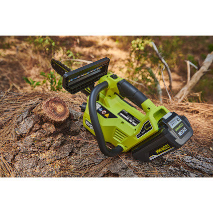 Grön batteridriven topphandsåg från Ryobi ligger på ett trädstam i skogsmiljö.