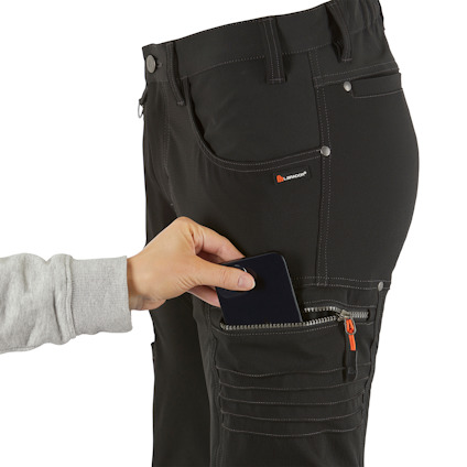 En person lägger en telefon i en benficka på svarta arbetsbyxor med orange dragkedjor.
