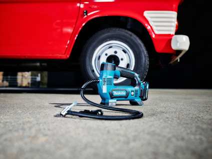 En blå och svart luftpump ligger på marken framför ett rött fordon med ett vit däck.