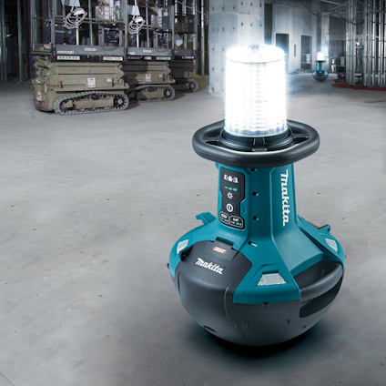 Portabel arbetslampa i en industriell miljö, ljussken, märkning "Makita". Plattform och utrustning i bakgrunden.