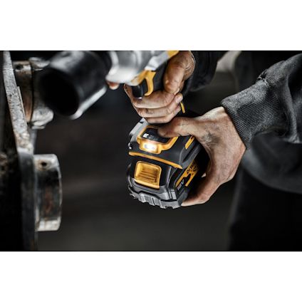 Person håller en gul och svart sladdlös borrmaskin och pressar den mot en metallbit.