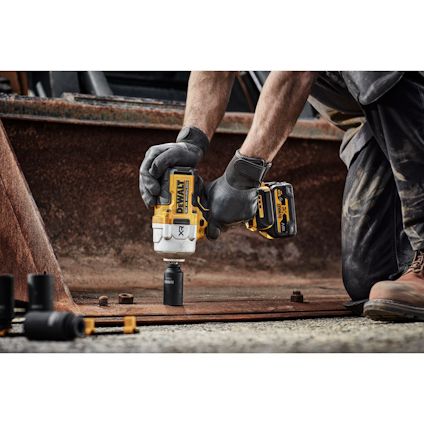 En person i arbetshandskar använder en DeWalt-borrmaskin för att borra i metall. Andra borrdelar är synliga i förgrunden.