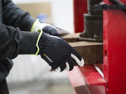 Person med svarta handskar hanterar ett metallföremål i en industriell miljö.