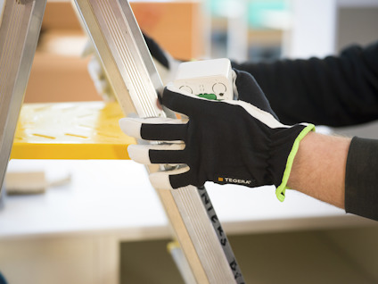 En hand i arbetshandske håller i en del av en stege.