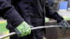 Person med gröna handskar böjer metallstång.