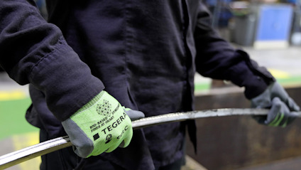 Person med svarta kläder håller i ett metallrör med gröna handskar märkta "TEGERA".