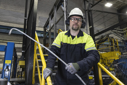 Man i skyddsutrustning med stång, industriell miljö, säkerhetsskydd runt arbetsområde.