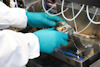 Person med blå handskar justerar metallutrustning med flera kablar i en laboratoriemiljö.