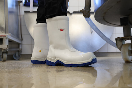 Vita stövlar med blå sula på ett vått golv i en industriell miljö.