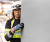 Person med hjälm och skyddsglasögon håller i ett stort skivmaterial.