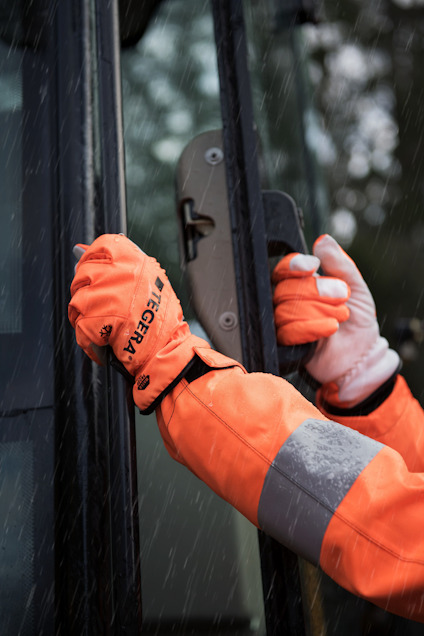 Person i orange arbetskläder och handskar öppnar en dörr i regn.