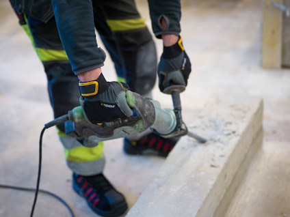Person i arbetskläder använder en slagborr på betongyta.