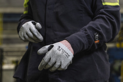 Person with grey work gloves and dark clothing in an industrial setting.
