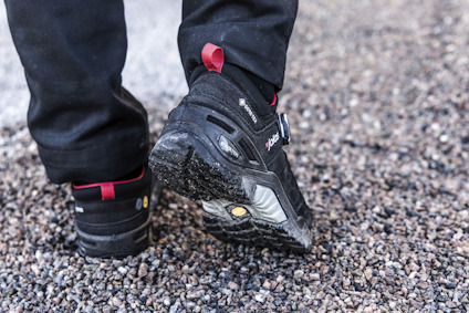 Svarta arbetsstövlar med dragsnoddar, synliga på grusunderlag.