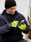 En person med mössa och handskar använder en mobiltelefon vid en vit bil.
