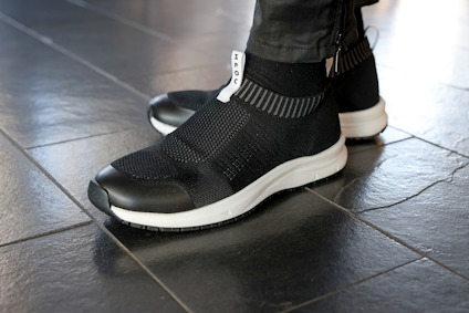 Svarta sneakers med vit sula på svart kakelgolv. En person bär skorna.