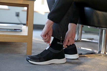 Person som drar upp sina byxor för att visa svarta strumpor och svarta sneakers med vita sulor, sittande inomhus.