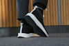 Svart sneaker med vit sula och text "Echø" på hälen, på grå matta och med träpanel i bakgrunden.
