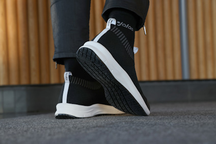 Svart sneaker med vit sula och text "Echø" på hälen, på grå matta och med träpanel i bakgrunden.