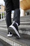Person går uppför trappa, klädd i svarta byxor och svarta sneakers med vit sula.