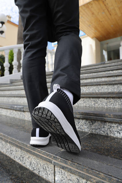 Person går uppför trappa, klädd i svarta byxor och svarta sneakers med vit sula.