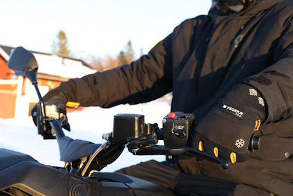 Person in black clothing on a motorcycle with snow in the background, wearing gloves with snowflake symbols.
