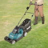 Gräsklippare av märket Makita på gräsmatta, person i stövlar och beige kläder skjuter den.