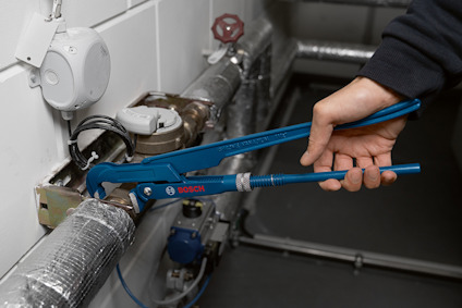 Blå polygripverktyg används för att greppa ett metallrör i ett rum med teknisk utrustning och kablar.