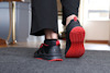 En person går på en matta med svarta sneakers som har röda sulor och detaljer.