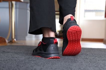 En person går på en matta med svarta sneakers som har röda sulor och detaljer.