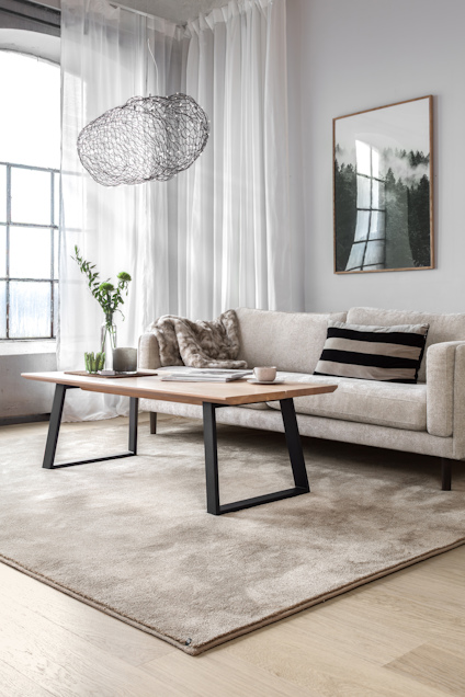 Vardagsrum med beige soffa, trärustikt soffbord, randig kudde, lurvig kudde, växtvas och taklampa av metalltråd.