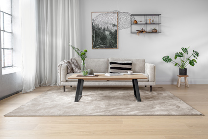 Soffa med beige kudde, träsoffa med svarta ben, växt i kruka, väggdekoration med spegel och hyllor, vitrinskåp till vänster.