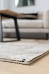 Beige matta på ljust trägolv, soffbord och soffa i bakgrunden. Avslappnad interiörstil.