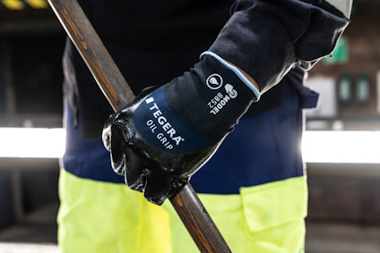 Hand med svart handske håller ett metallrör, handsken märkt "TEGERA OIL GRIP".