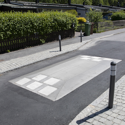 Farthinder i asfalt på en villagata omgiven av häckar och trottoarer med kantsten.